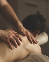 Fototapeta na wymiar Woman is getting massage. Back massage. Dark-haired woman lies face down on couch. Masseur's hands on back. Relax, spa, body care. Side view. Soft focus.