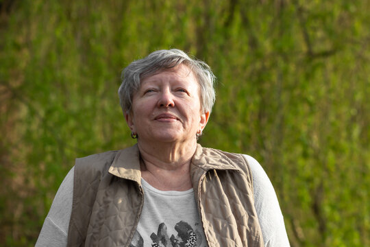 Happy Senior Woman Relaxing And Breathing Fresh Air In Spring Park, Green Nature Background. Grandma Meditation In Park.