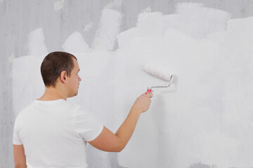 rear view of painter man painting wall into white with paint roller