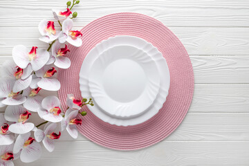 Festive place setting with pink napkin and orchid flowers. Empty plates on white wooden table. Top view. Festive dinner. Card or menu template, flat design. Copy space. Mockup, layout. Floral frame.