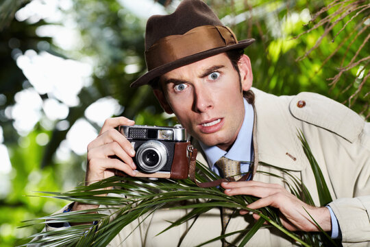 Retro spy man, camera and jungle for investigation, inspection or journalist with shock at job. Private investigator, secret photographer and retro paparazzi in trees, bush or leaves for surveillance