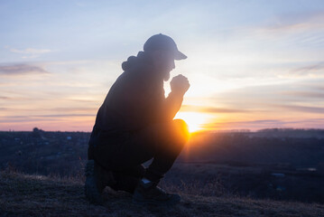 Man on his knees praying. On the background of the sunset sky. Kneeling Prayer to God. Worship and praise.