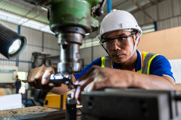 Asian worker man wearing uniform safety and hardhat uses a vernier measuring machine to inspect components for fabrication in factory industrial, worker manufactory industry concept.