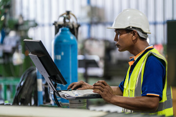 Asian engineer or worker is using a computer to control a steel laser cutting machine in a factory. Real worker.