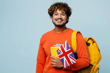 Gordijnen Young smiling happy fun teen Indian boy student wears casual clothes backpack bag hold books British flag isolated on plain pastel light blue cyan background. High school university college concept. © ViDi Studio