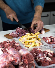 A man prepares various raw meats, bones and offal for freezing. BARF Biologically Appropriate Raw Food for Dogs and Cats. Animal food packaging.