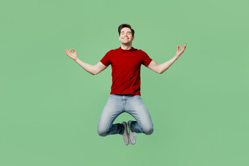 Fototapeta na wymiar Full body young spiritual man he wears red t-shirt casual clothes jump high hold spreading hands in yoga om aum gesture relax meditate try to calm down isolated on plain pastel light green background.
