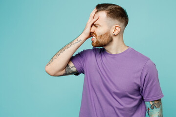 Young sad man he wearing purple t-shirt put hand on face facepalm epic fail mistaken omg gesture isolated on plain pastel light blue cyan background studio portrait. Tattoo translates life is fight.