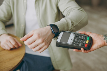 Cropped young man wearing casual clothes sits alone at table in coffee shop cafe indoors work or study on laptop pc computer hold bank terminal process acquire smart watch payment Freelance concept.