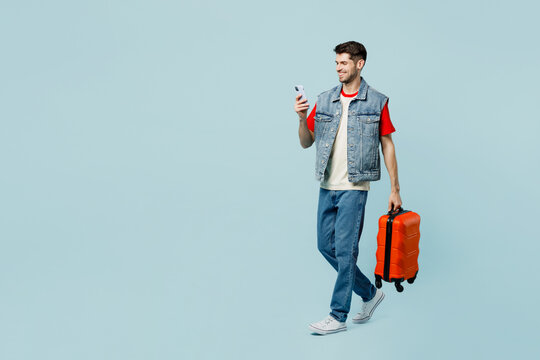 Traveler man in casual clothes hold suitcase use mobile cell phone isolated on plain pastel blue cyan background Tourist travel abroad in free spare time rest getaway Air flight trip journey concept