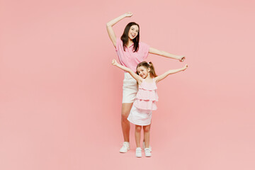 Full body smiling happy woman wear casual clothes with child kid girl 6-7 years old. Mother stand behind daughter, raise up hands isolated on plain pastel pink background. Family parent day concept.