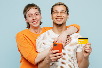 Young couple two gay men wear casual clothes together use mobile cell phone credit bank card shopping online isolated on plain blue background studio portrait. Pride day june month love LGBTQ concept.