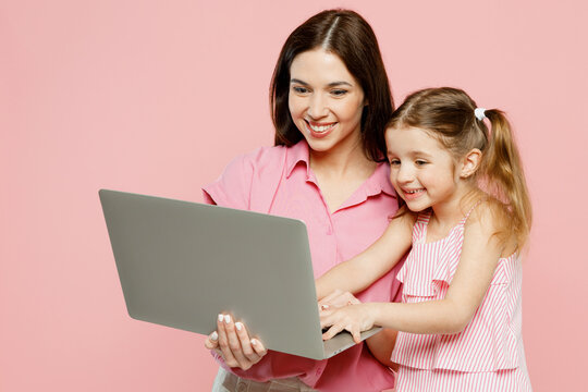 Happy cheerful IT woman wear casual clothes with child kid girl 6-7 years old. Mother daughter hold use work on laptop pc computer isolated on plain pastel pink background. Family parent day concept.