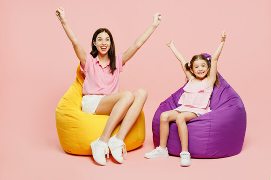 Full body woman wear casual clothes with child kid girl 6-7 years old. Mother daughter sit in bag chair do winer gesture look camera isolated on plain pastel pink background Family parent day concept