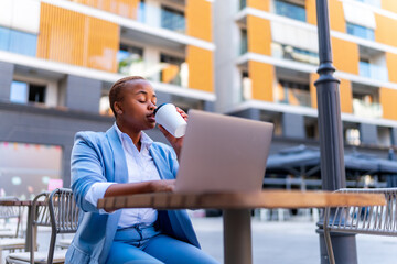 The intern uses the break to catch up on assignments using her laptop while sitting in a cafe drinking coffee