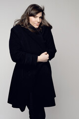 Woman, fashion and portrait of plus size model posing in winter clothing against a grey studio background. Isolated female person standing with stylish black coat, body or warm fashionable clothes