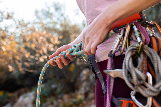 climber tying a knot before climbing. Close-up of a rock climber in harness and climbing equipment outdoors.