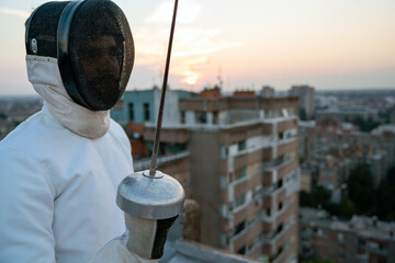Woman in white fencing costume practicing outdoors. Sport, professional coach, healthy lifestyle.