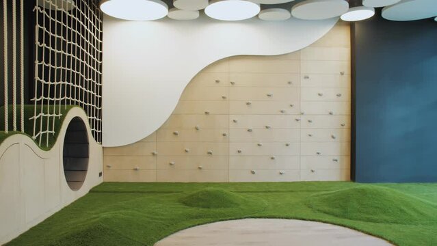 Dolly shot of empty game room indoor with rounded ceiling, green lawn and climbing wall for children, slow motion.