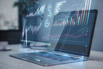Close up of laptop on desktop with abstract glowing candlestick business chart on blurry...