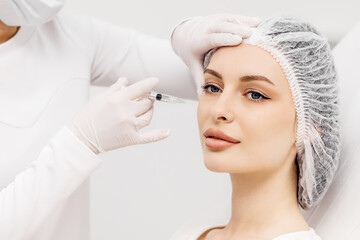 Skin lifting injection. A young woman is receiving a Botox injection in her forehead while lying on a white background. The concept of prolonging youth and cosmetology
