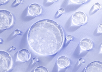 round drops of transparent gel serum on purple background