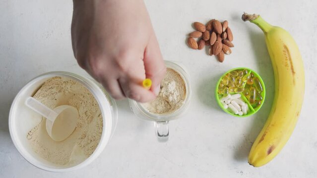 Male hand with a straw mixing white whey or soy protein powder in a glass jar with milk banana smoothie, sport nutrition, top view