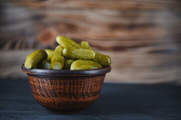 Pickled gherkins or cucumbers in bowl on wooden rustic table from above.