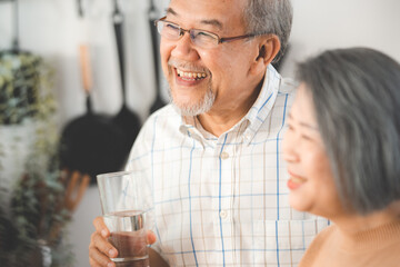 Family health care in house concept, Asian senior elderly couple drink a glass of water in kitchen room at home, Mature older thirsty grandparent holding clean mineral natural in glass, peace of mind