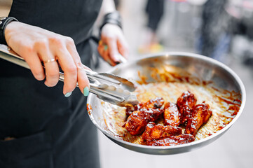woman chef cooking chicken wings in a sauce in the kitchen