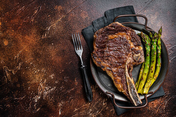 BBQ Grilled Tomahawk or Cowboy with bone beef steak, roasted asparagus. Wooden background. Top...