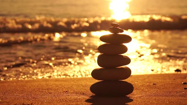Balanced rock pyramid on pebbles beach, sunny day and clear sky at sunset. Golden sea bokeh on background. Selective focus, zen stones on sea beach, meditation, spa, harmony, calm, balance concept.