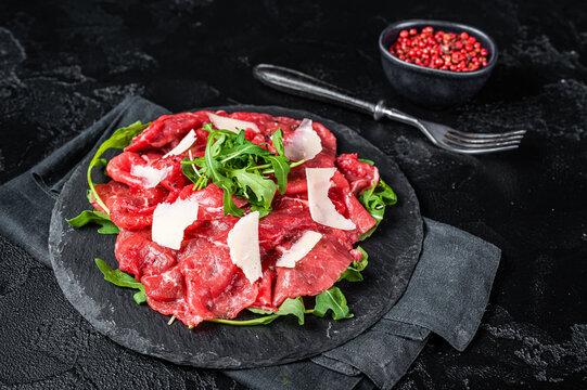 Beef carpaccio with arugula, parmesan cheese. Black background. Top view
