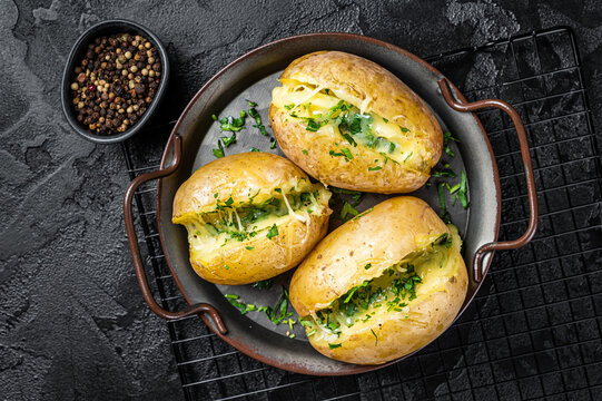 Baked Jacket potatoes with cheese, herbs and butter. Black background. Top view