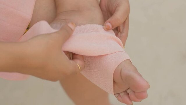 A woman applying bandage to her sprained ankle, workout injury, leg closeup
