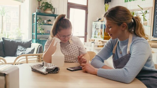 Down syndrome girl browsing phone together with her workmate during the break in the cafe. Shot with RED helium camera in 8K. 
