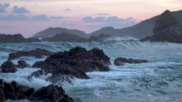 Rocky rugged beach in Baja California Mexico west coast with ocean waves splashing and three swimmers right, Wide handheld shot