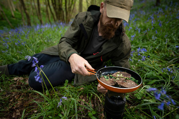 A man cooking steak and wild garlic in a bluebell woodland while wild camping