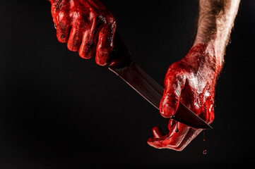 A man wipes a bloody knife with his hand on a black background. 