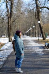 Smiling young woman in blue parka walking at park at sunny spring day.