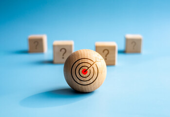 Wood sphere with target icon in front of the wooden cube blocks with question mark symbol on blue background. Concept of leadership, business target and success, motivation and definite chief aim.