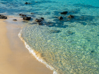 Calm beach scene, movement of blue sea water and wave surf, group of rocks on clean sandy beach...