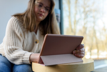 Fototapeta premium Young Woman in knitted sweater and glasses drawing or working on tablet pc
