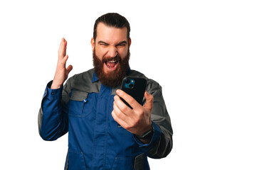 Upset young bearded handy man is screaming at the phone he is holding. Studio shot over white background.