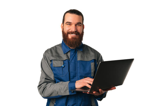 Wide smiling bearded man wearing engineer uniform is holding a laptop over white background.