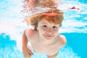 Fototapeta na wymiar Summer kids in water in pool underwater. Funny kids face underwater. Young boy swim and dive underwater. Under water portrait in swim pool. Child boy diving into a swimming pool.