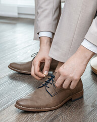 The groom is sitting in a beige suit, straightening his tie, tying his shoelaces, wedding, beige...