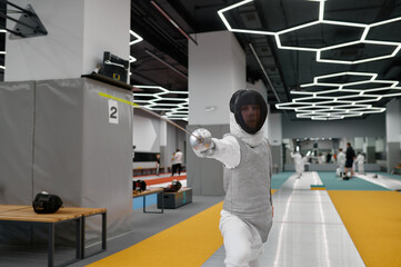 Young fencer practicing attack in training room after lesson