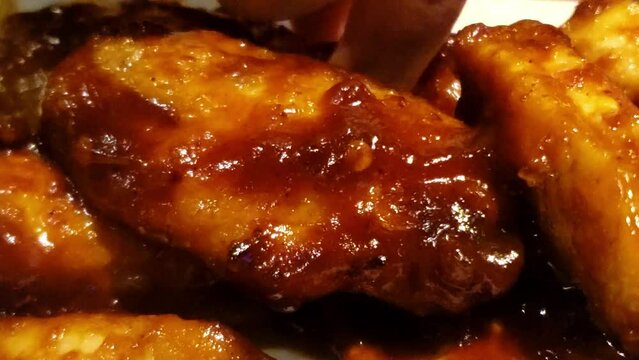 chicken wings bbq sauce zoom into ladies finger reaches in to grab a drum of the sauce mark left on white plate in a tasty pile of juicy fresh served to enjoy at fast food pub for casual appetizers