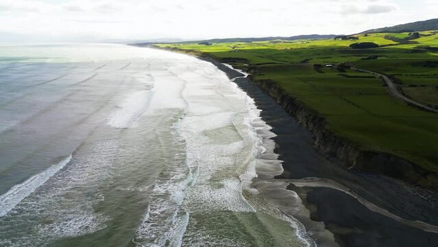 Black gemstone ocean beach with cliffs and lush green meadow in New Zealand